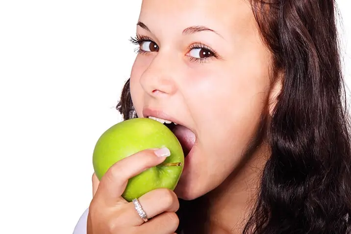 Young woman biting into a green apple.