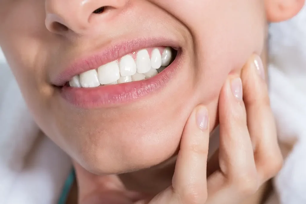 Close up of womans mouth showing teeth and their hand grabbing their face in pain
