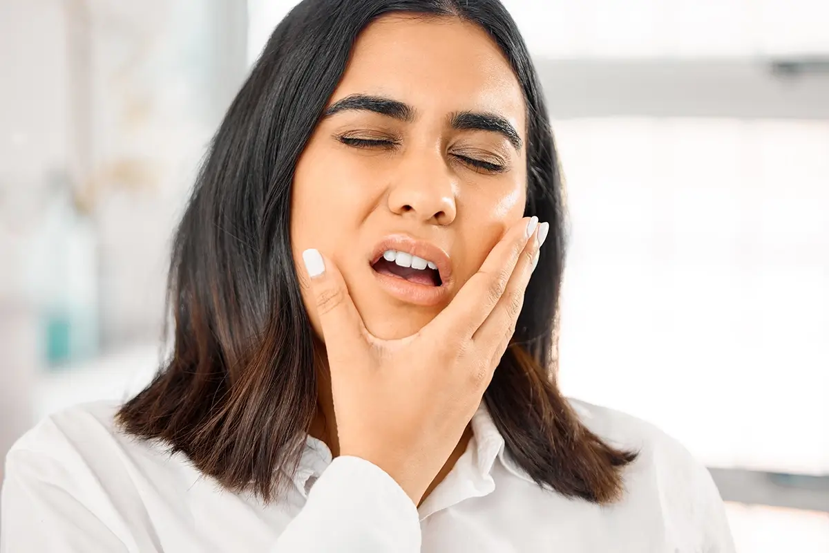Woman looking uncomfortable holding her chin and side of her face.